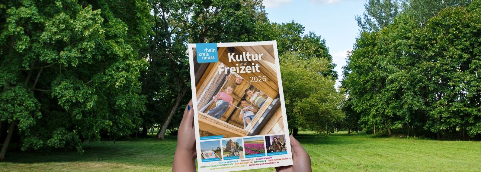 Eine Hand hält einen Kultur- und Freizeitführer für den Rhein-Kreis Neuss aus dem Jahr 2026 vor einem Hintergrund aus Bäumen und Gras. Der Slogan "Neuerscheinung" ist prominent platziert.